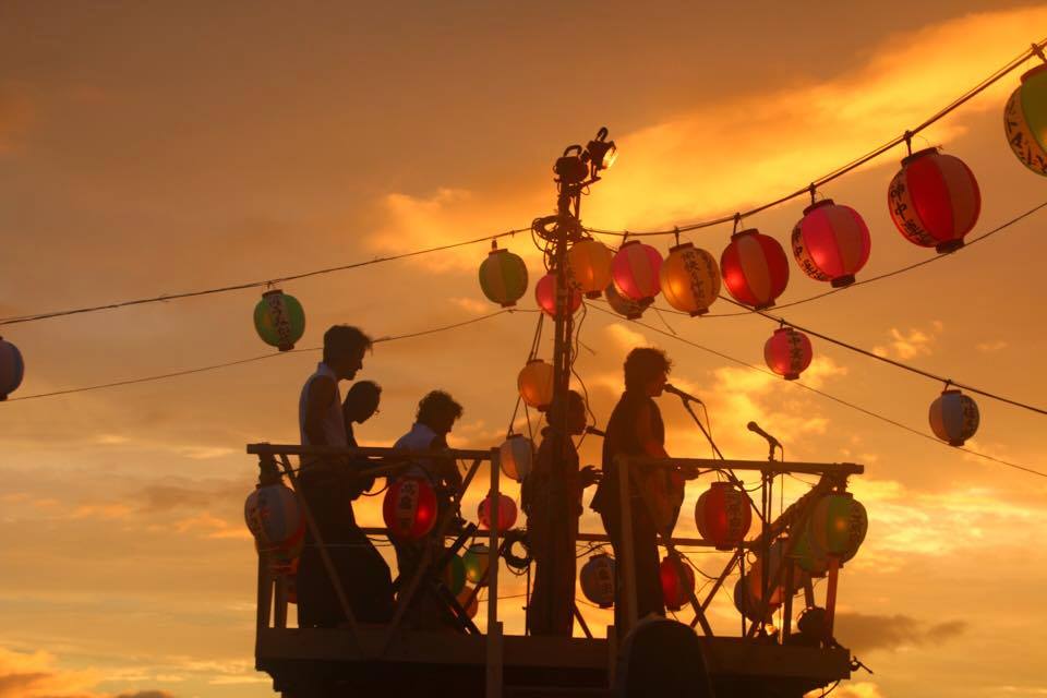 鎌倉・材木座の盆踊り大会で砂浜に組まれた櫓の上で演奏する小川コータさん