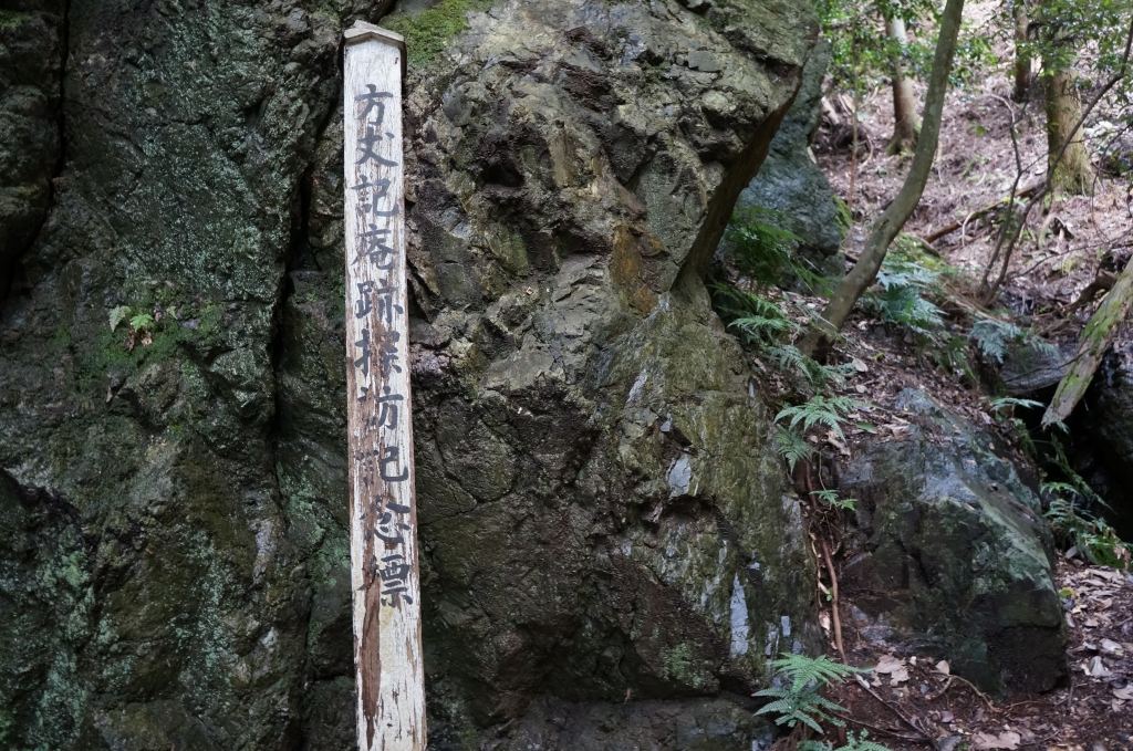 山中の岩の前に立つ方丈庵跡の標柱