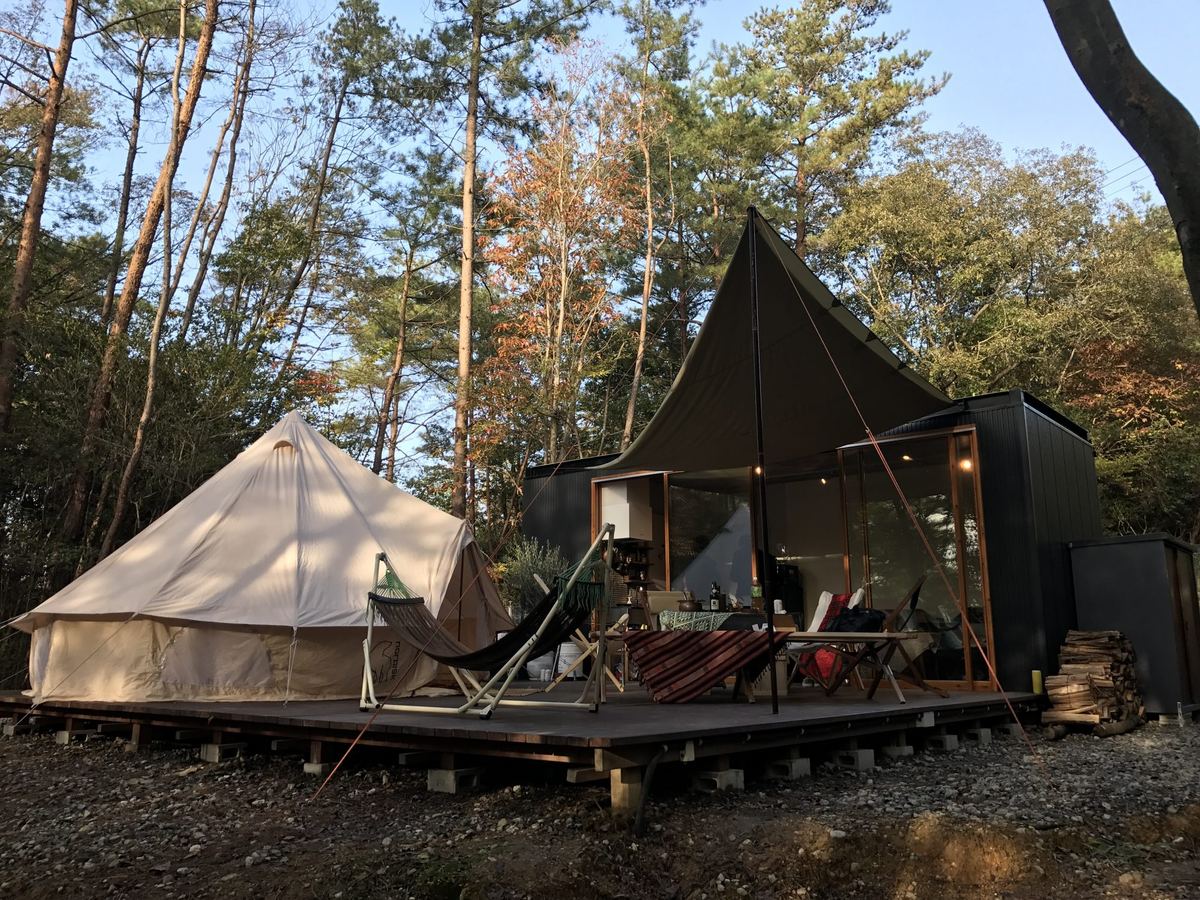 森の中のウッドデッキに置かれた黒い小屋とテント