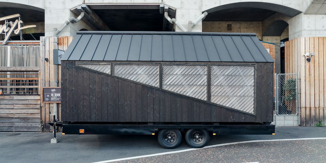 高架下に置かれた黒い外壁のトレーラーハウス「HAWK」