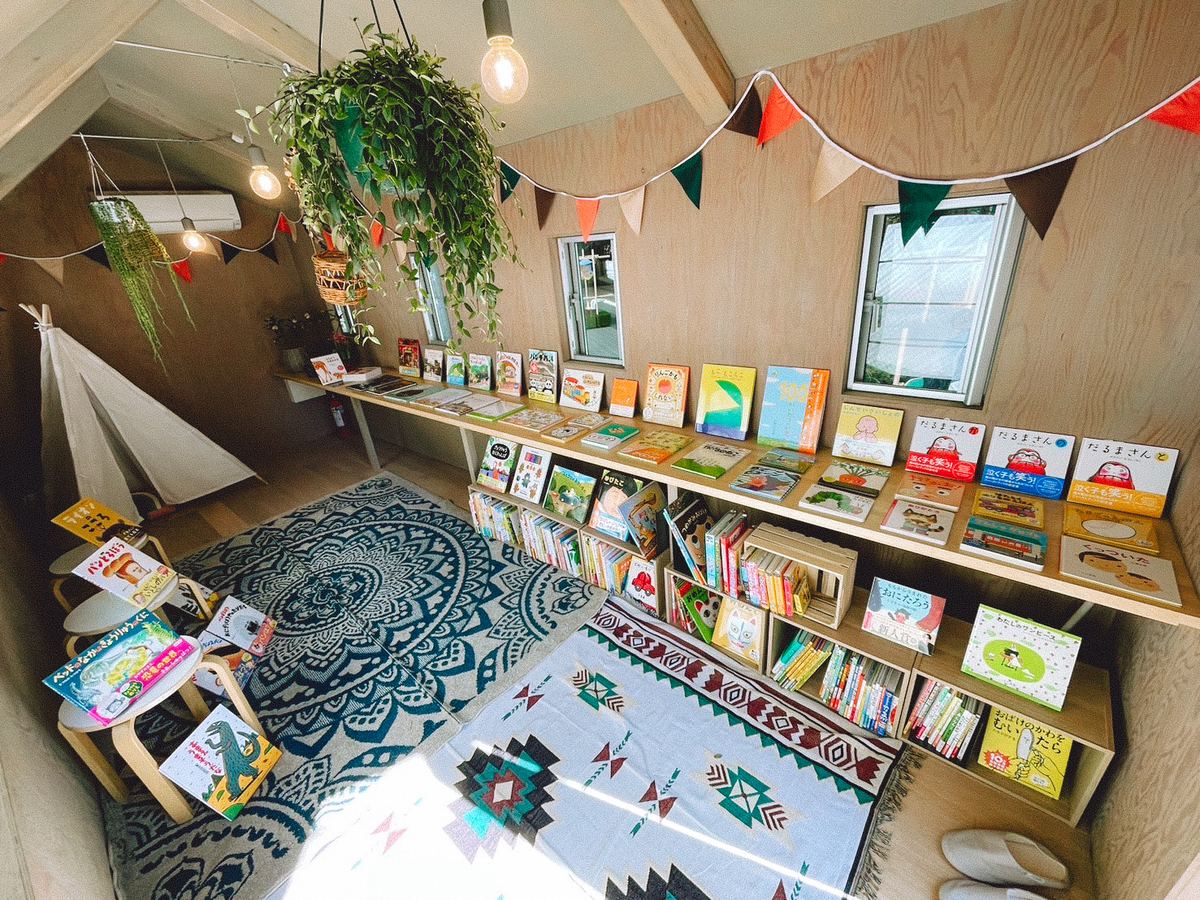 絵本が並ぶ本棚と敷物のある、小屋の室内