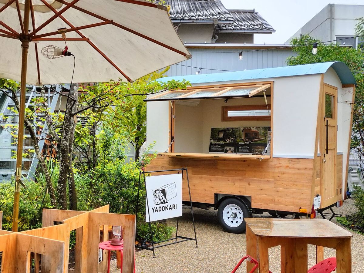 植栽とパラソルのそばに置かれ、窓を大きく開けて店として使われている小型トレーラーハウス
