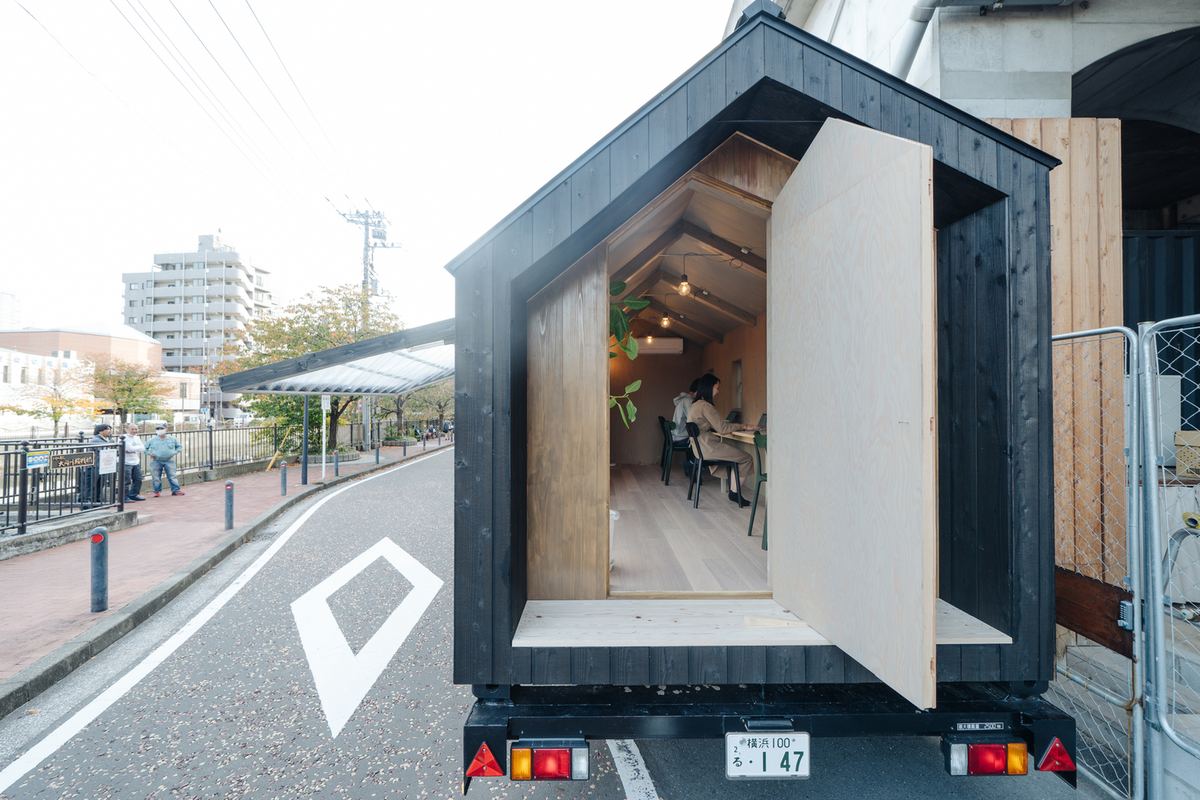 扉を開けた黒い外壁のトレーラーハウスのオフィス