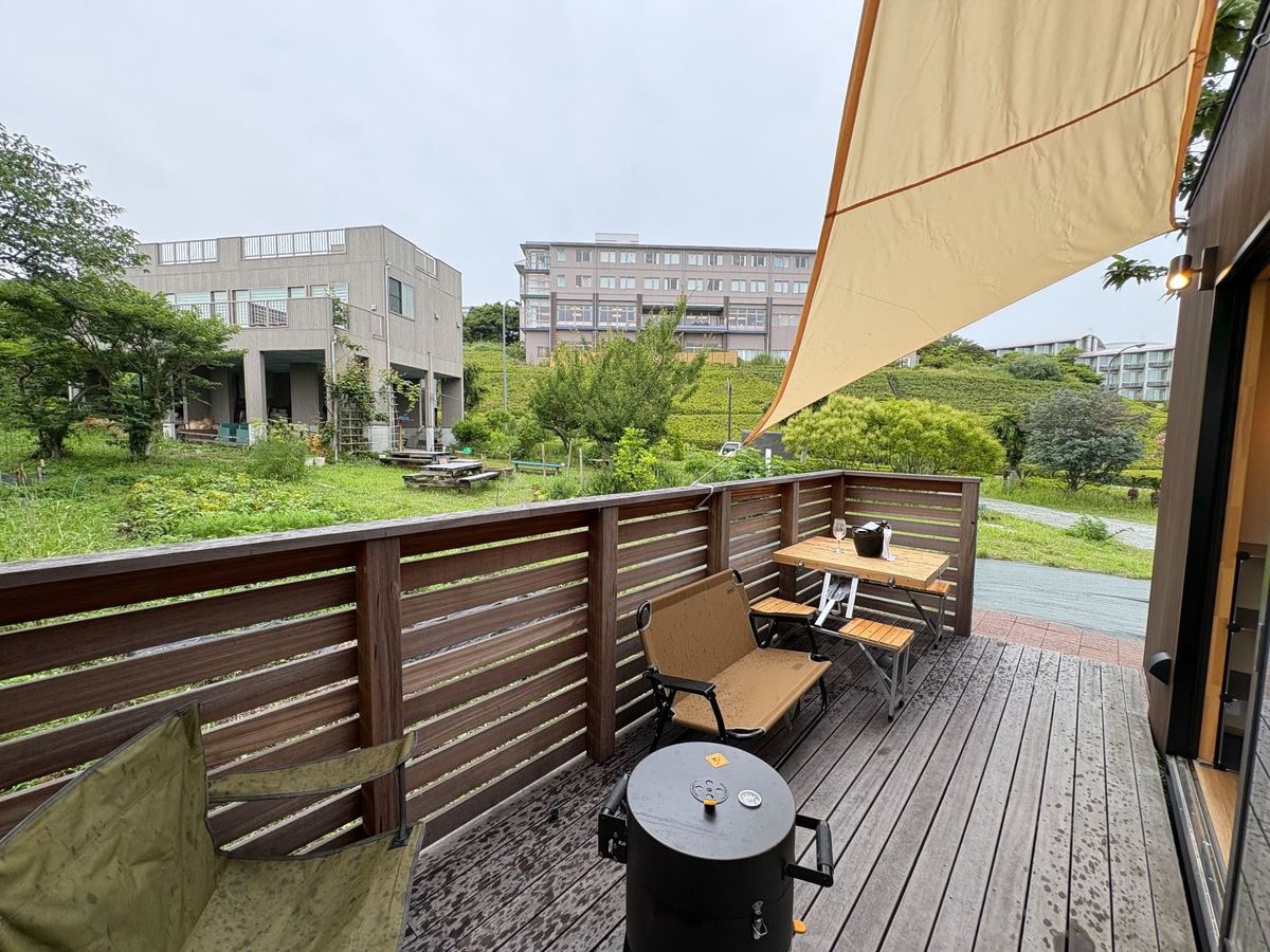 タープを張ったウッドデッキから見た、緑の庭と周りの建物