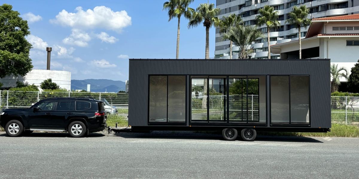 車で牽引して運ばれる黒いトレーラーハウス
