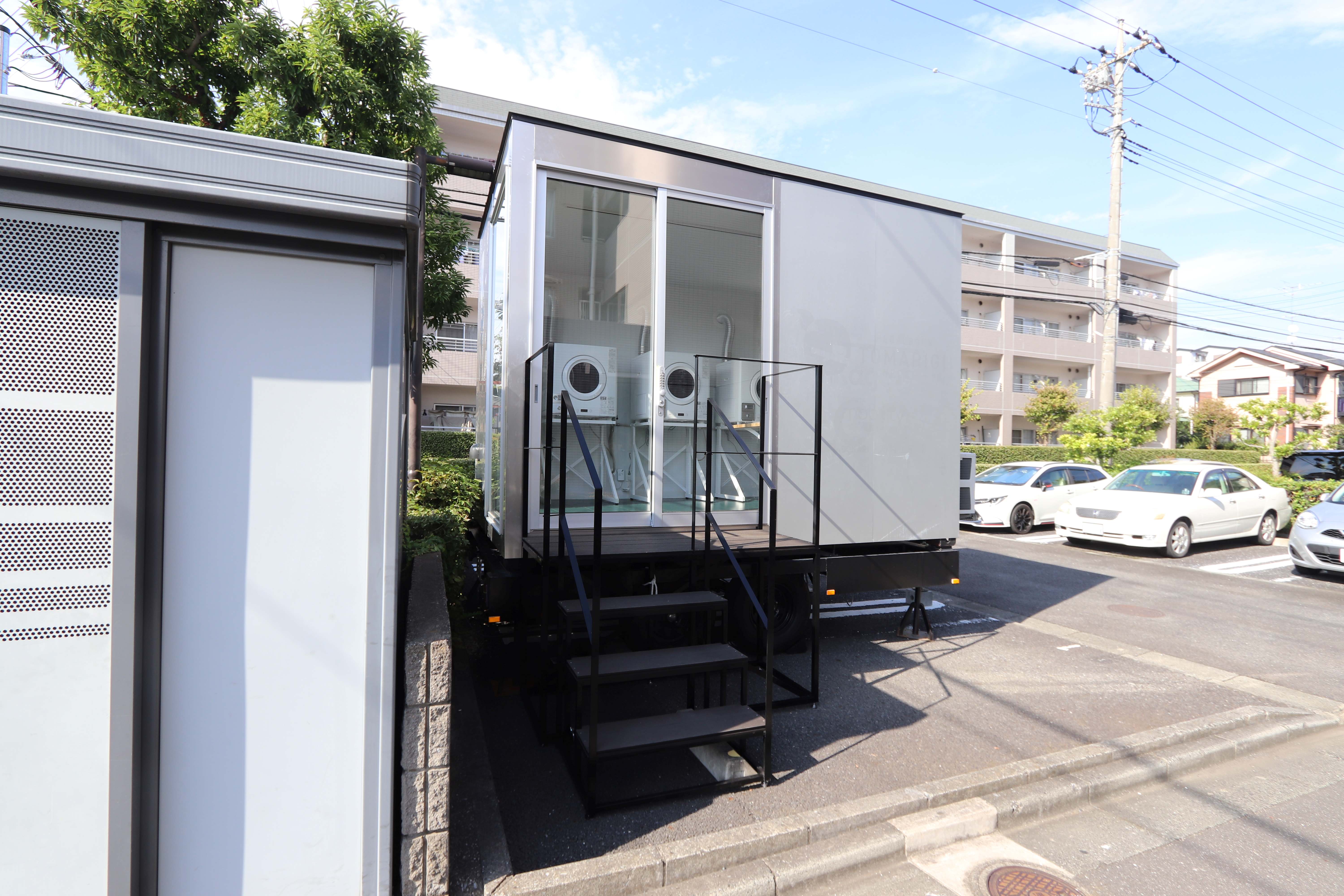 駐車場の脇に置かれ、階段を付けた白いトレーラーハウス