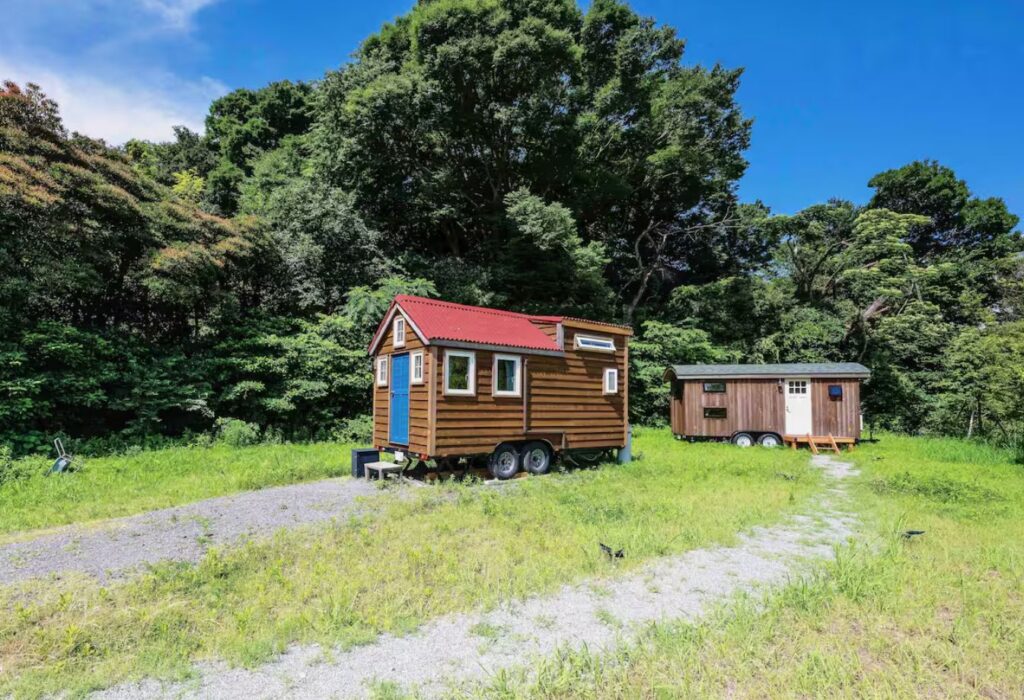 森を背にした草地に置かれた、赤い屋根と木の外壁のタイニーハウス