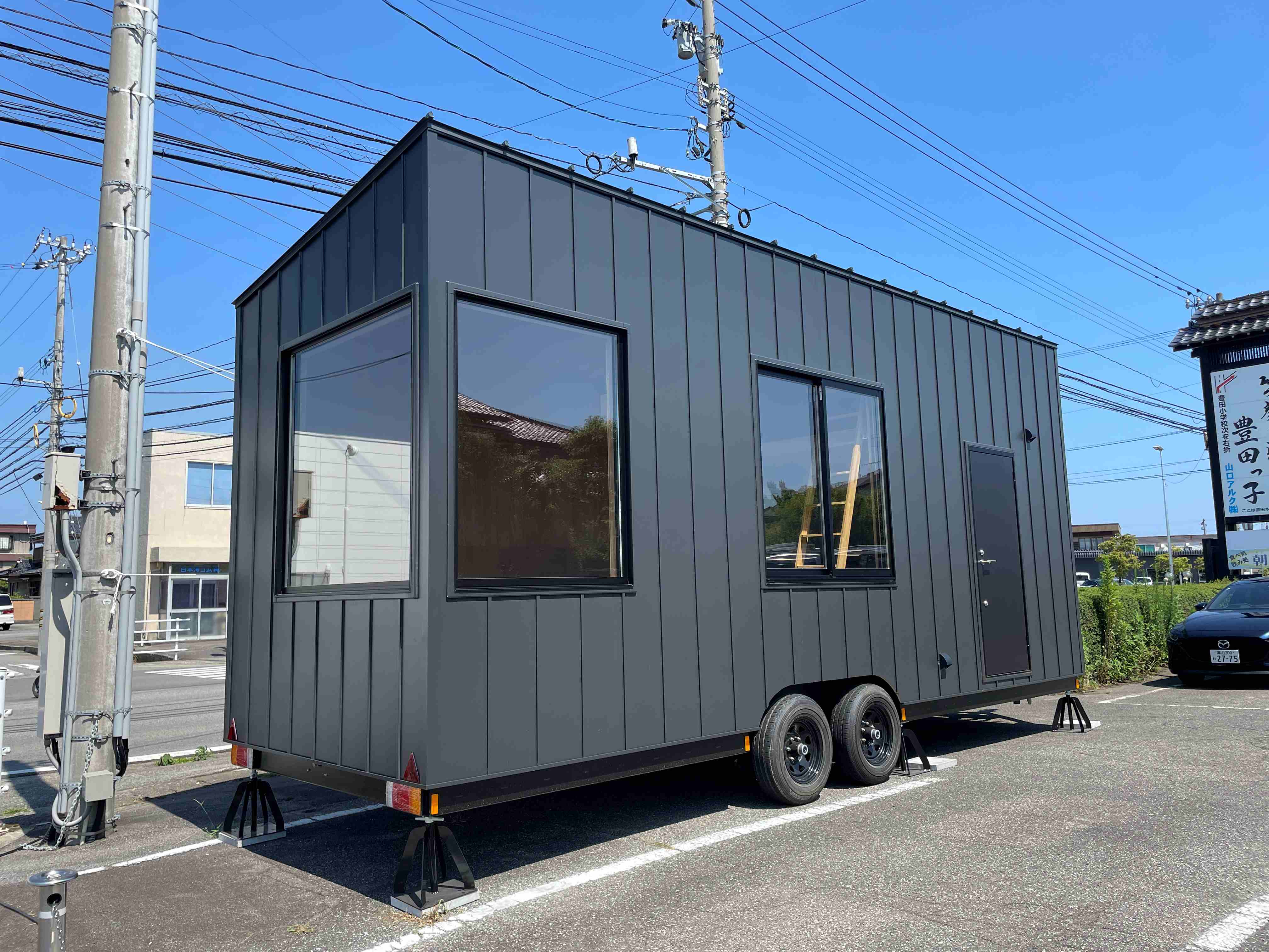 車輪を付けたまま、ジャッキで支えて置かれた黒い外壁のトレーラーハウス