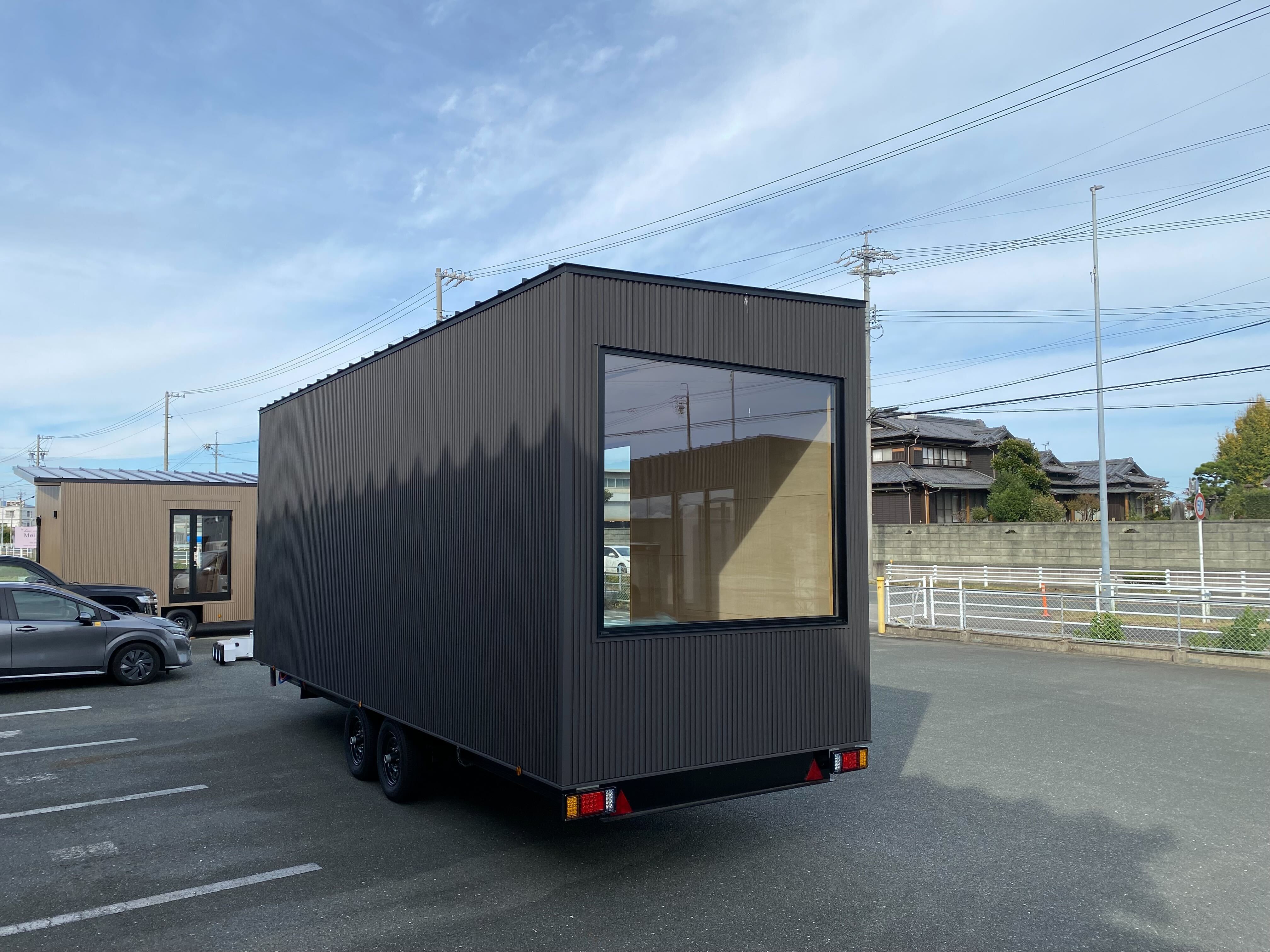 駐車場に置かれた黒い外壁のトレーラーハウス（Tinys INSPIRATION 7.2m）