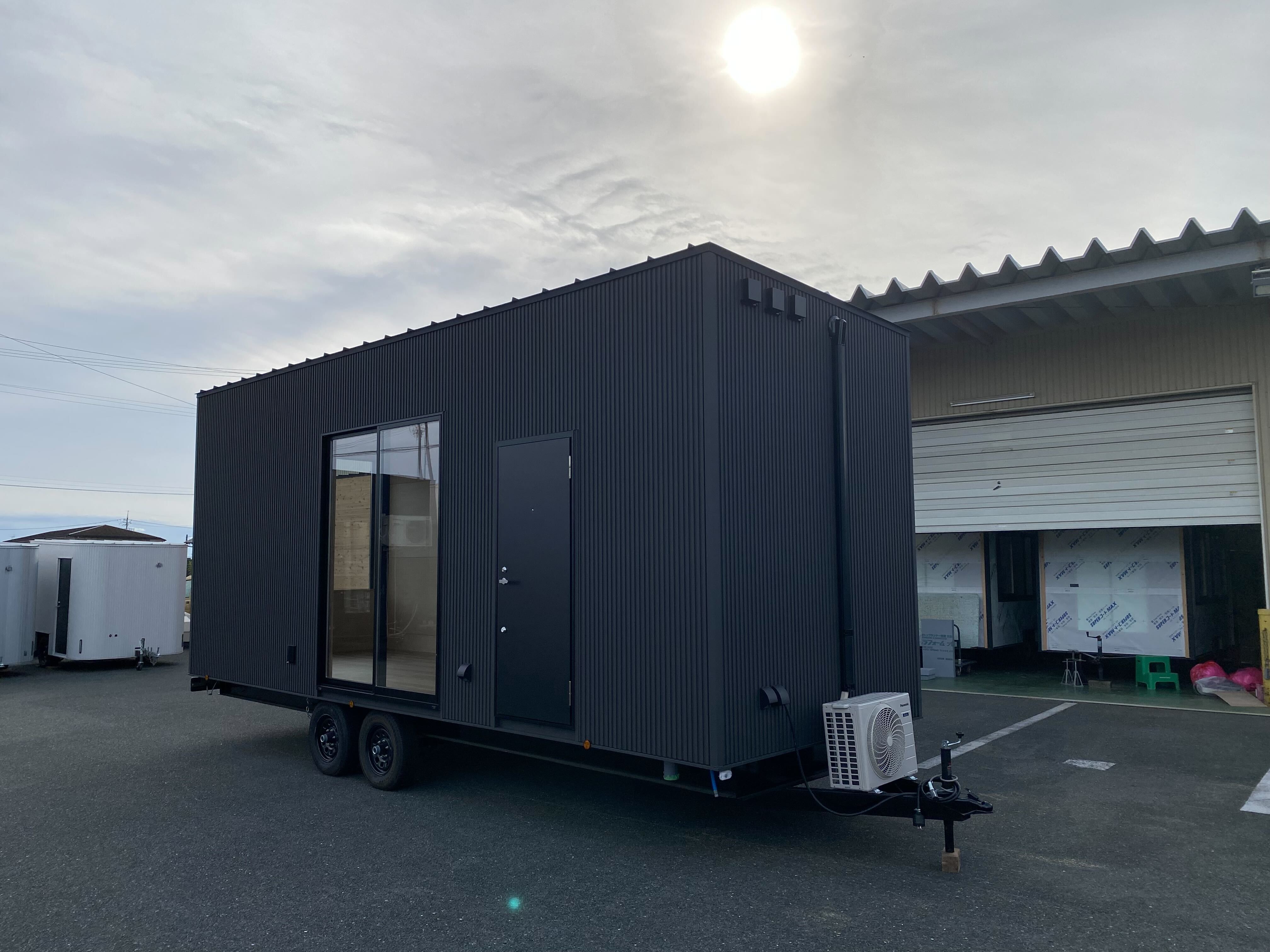 駐車場に置かれた、黒い外壁のトレーラーハウス（Tinys INSPIRATION 7.2m）